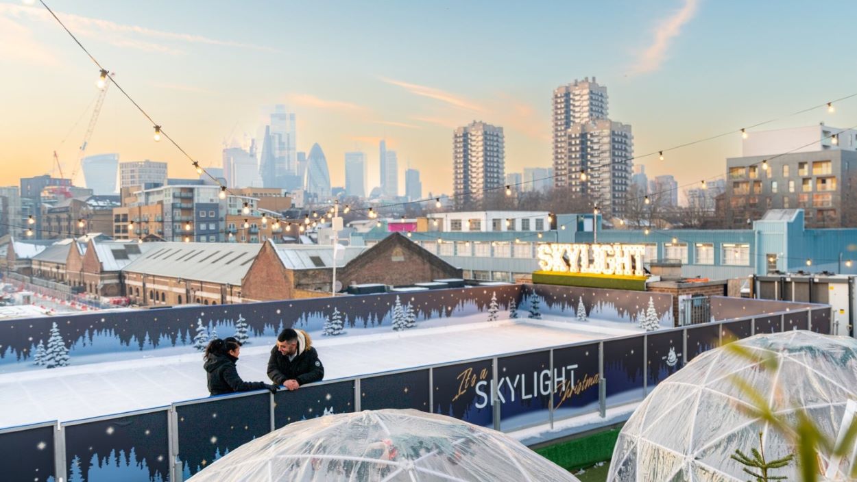 A couple talking on top of a rooftop ice rink with views of London