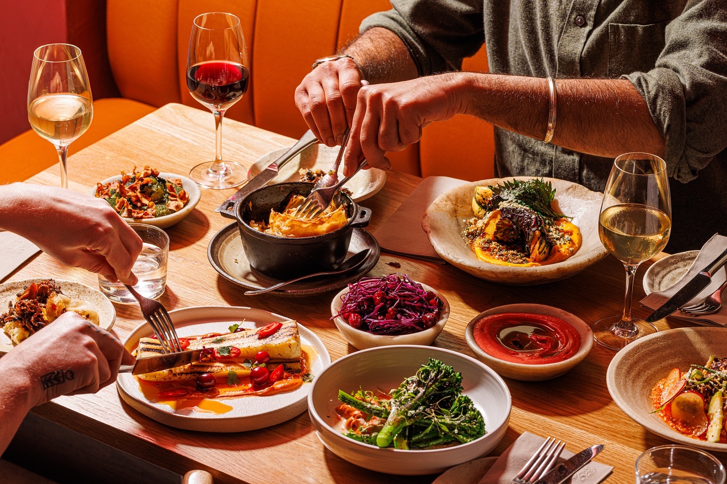 Two people eating at a dinner table, with wine, small plates, and delicious food.